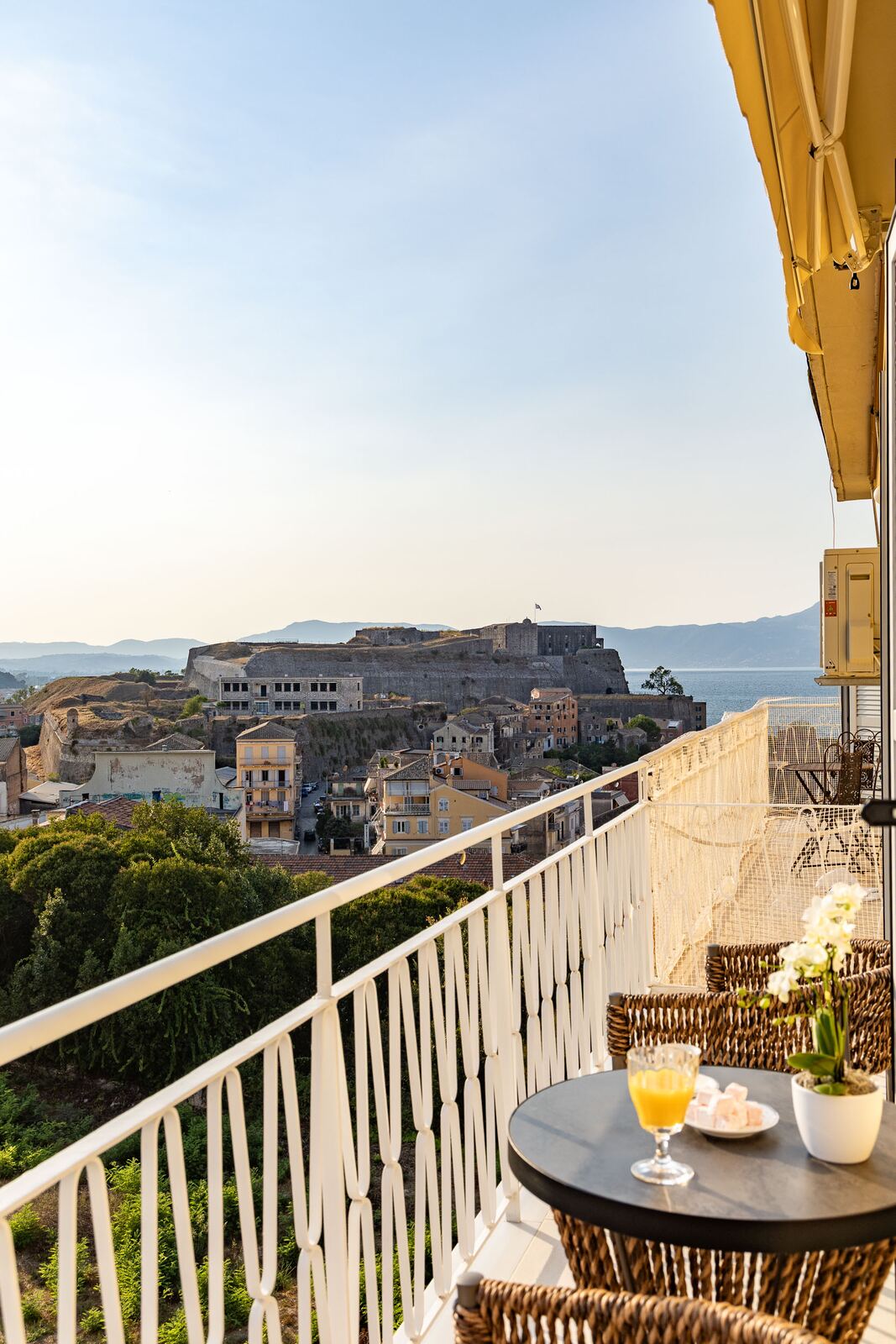 The balcony facing the New Fortress, table set with juice and loukoumia at golden hour