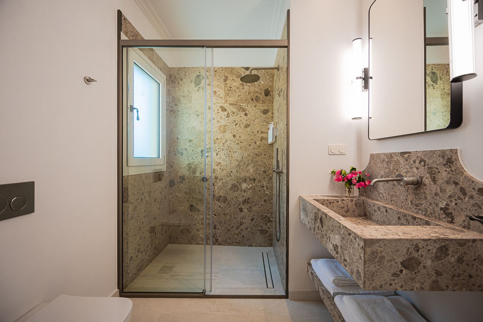 Bathroom in breccia stone with a walk-in glass shower and a carved stone basin
