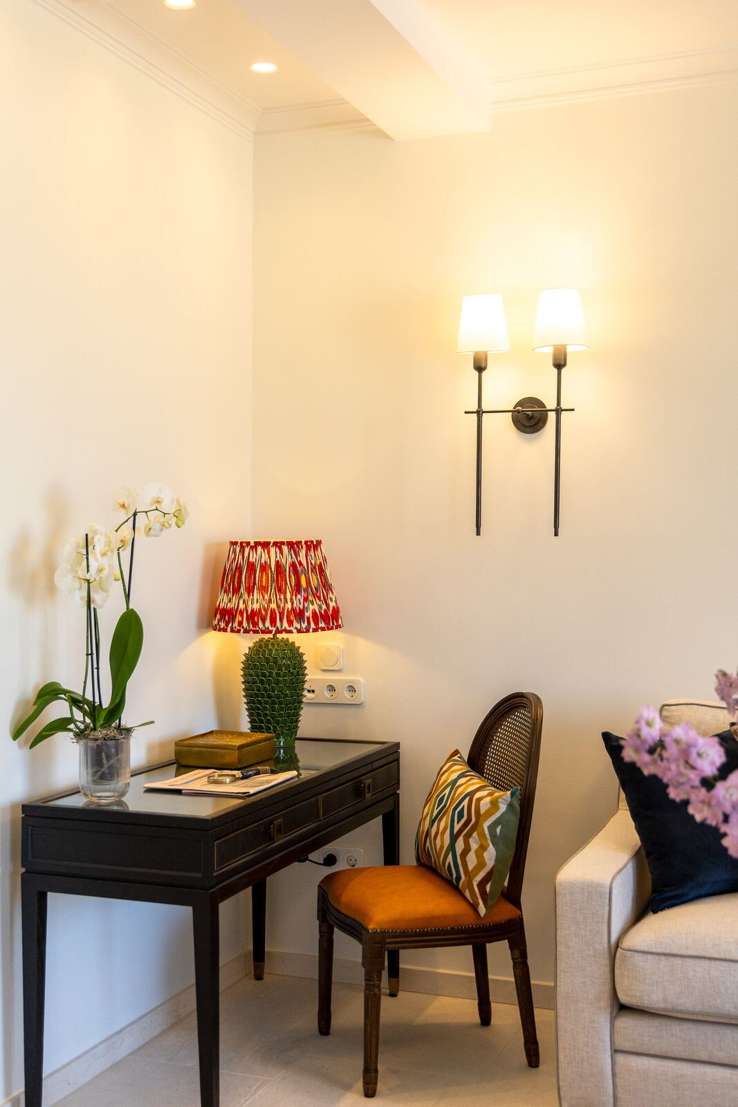 Writing desk with orchid and sconce beside the sofa