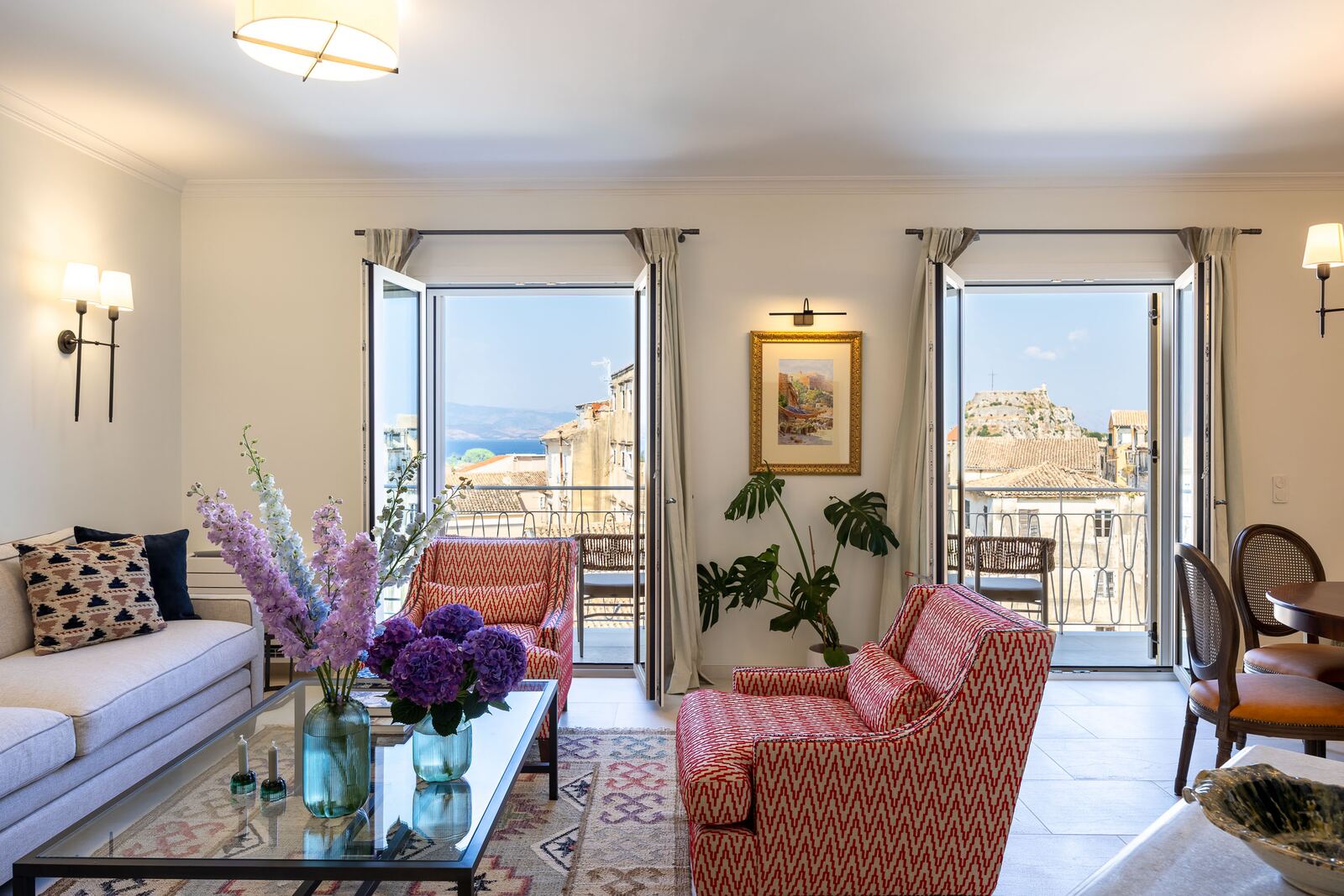 Living room at Terra di Corfu with linen sofa, coral armchairs and two sets of French doors open onto the balcony