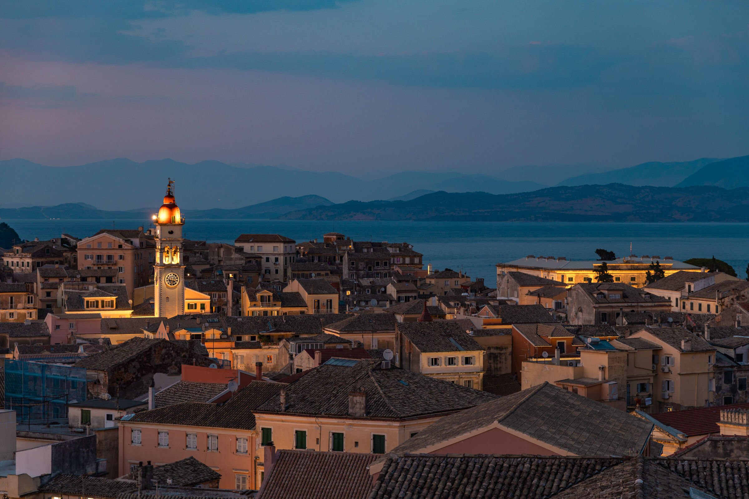 Corfu Old Town at dusk seen from the Terra di Corfu balcony, the bell tower of Agios Spyridon lit above the rooftops